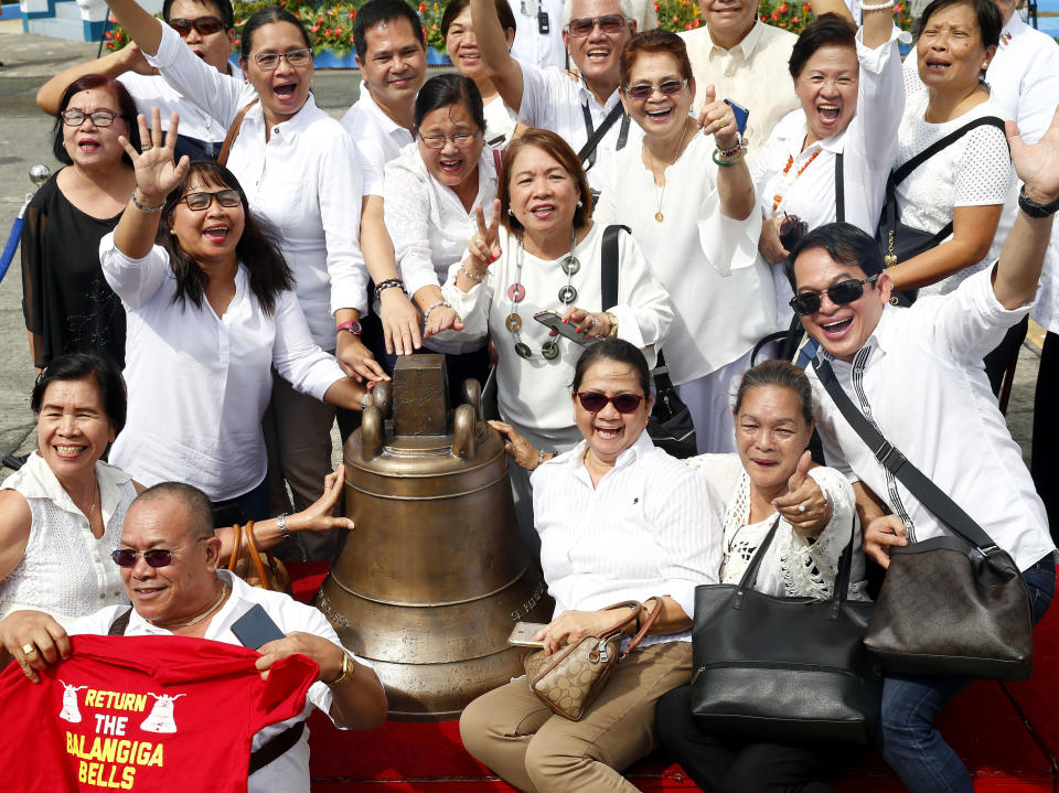 Residents from Balangiga township pose before one of three Balangiga church bells following handover ceremony upon their arrival Tuesday, Dec. 11, 2018 in suburban Pasay city, southeast of Manila, Philippines. American occupation troops took the bells in 1901 from a Catholic church following an attack by machete-wielding Filipino villagers, who killed 48 U.S. troops in the town of Balangiga on central Samar island in one of the U.S. Army's worst single-battle losses of that era. The bells are revered by Filipinos as symbols of national pride. (AP Photo/Bullit Marquez)