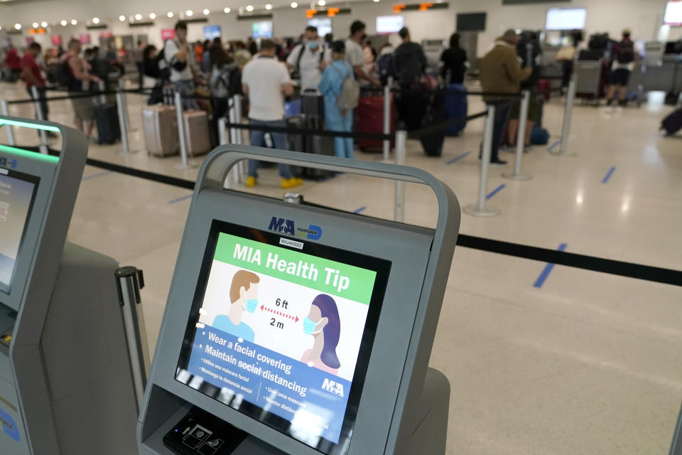 A kiosk displays a message encouraging wearing face masks and social distancing as passengers wait in line at Miami International Airport, Wednesday, Nov. 25, 2020, in Miami. (AP Photo/Lynne Sladky)