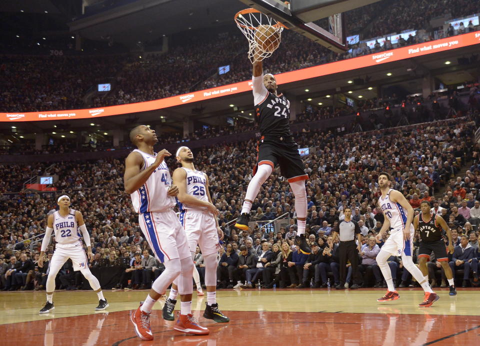 Toronto Raptors guard Norman Powell (24) slam dunks the ball past Philadelphia 76ers center Al Horford (42) and guard Ben Simmons (25) during the first half of an NBA basketball game, Wednesday, Jan. 22, 2020 in Toronto. (Nathan Denette/The Canadian Press via AP)