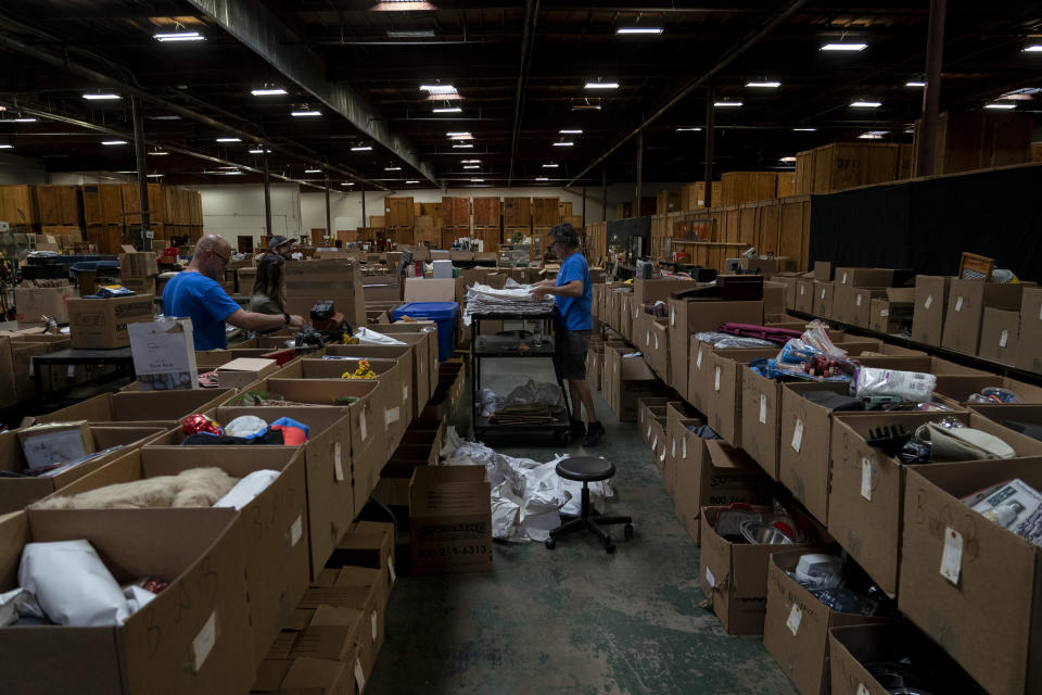 Auction workers sort items at a Los Angeles County warehouse in the County of Los Angeles, Calif., Thursday, June 15, 2023. The warehouse is filled with belongings from people's estates, including anything from doll collections and clothes to framed paintings, china dishware, washing machines, and cars, much of it housed in massive wooden crates. The items will be auctioned off to the public to pay off the estates' debts and cover burial or cremation services. (AP Photo/Jae C. Hong)