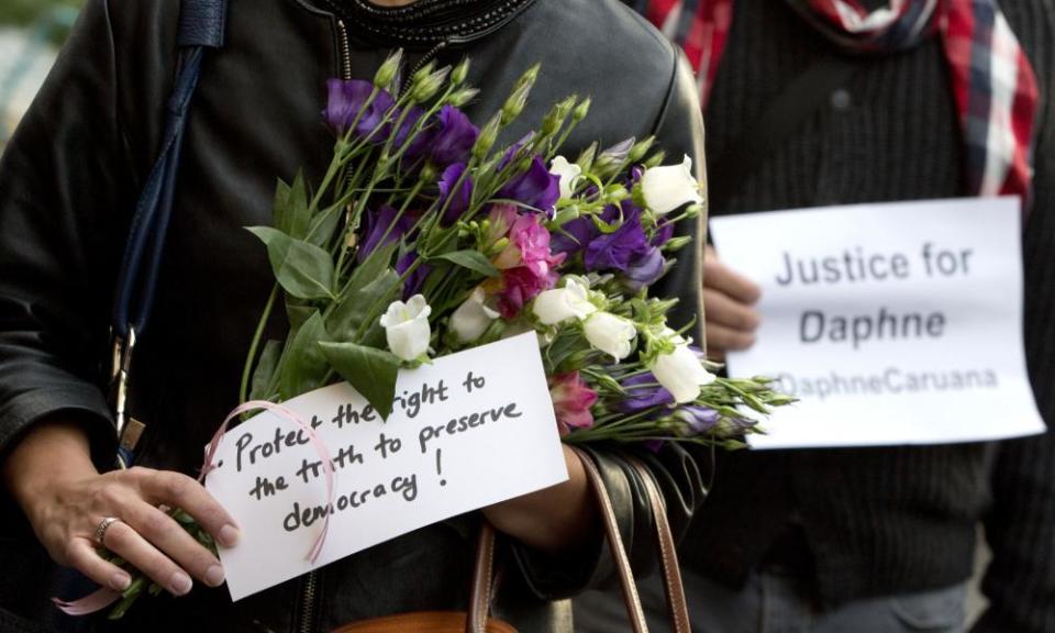 People hold flowers and signs outside EU headquarters in Brussels during a vigil for the journalist Daphne Caruana Galizia.