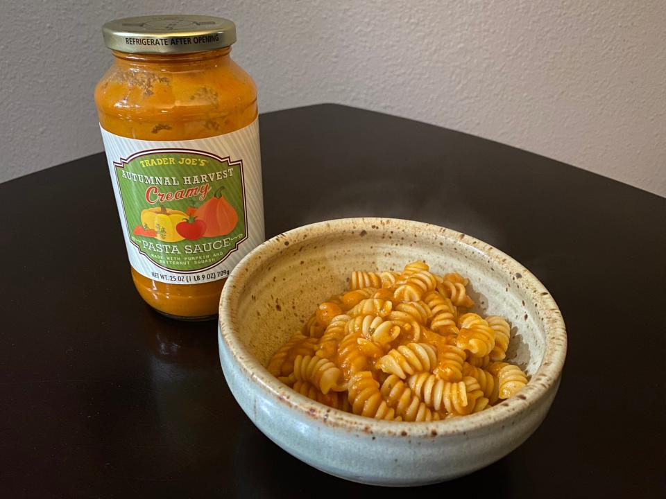 Pasta tossed in orange sauce with trader joe's autumnal harvest sauce in jar next to it