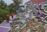 Members of police K-9 squad lead a sniffer dog during a search for victims at a hospital building collapsed in Friday's earthquake in Mamuju, West Sulawesi, Indonesia, Sunday, Jan. 17, 2021. Rescuers retrieved more bodies from the rubble of homes and buildings toppled by the 6.2 magnitude earthquake while military engineers managed to reopen ruptured roads to clear access for relief goods. (AP Photo/Yusuf Wahil)