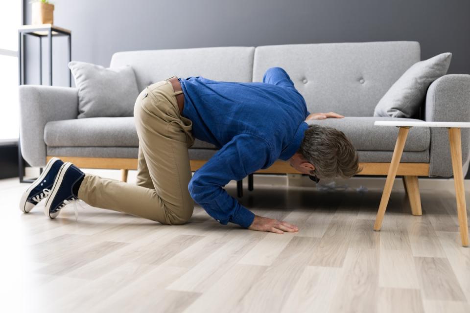 Man looking for a missing item under sofa.