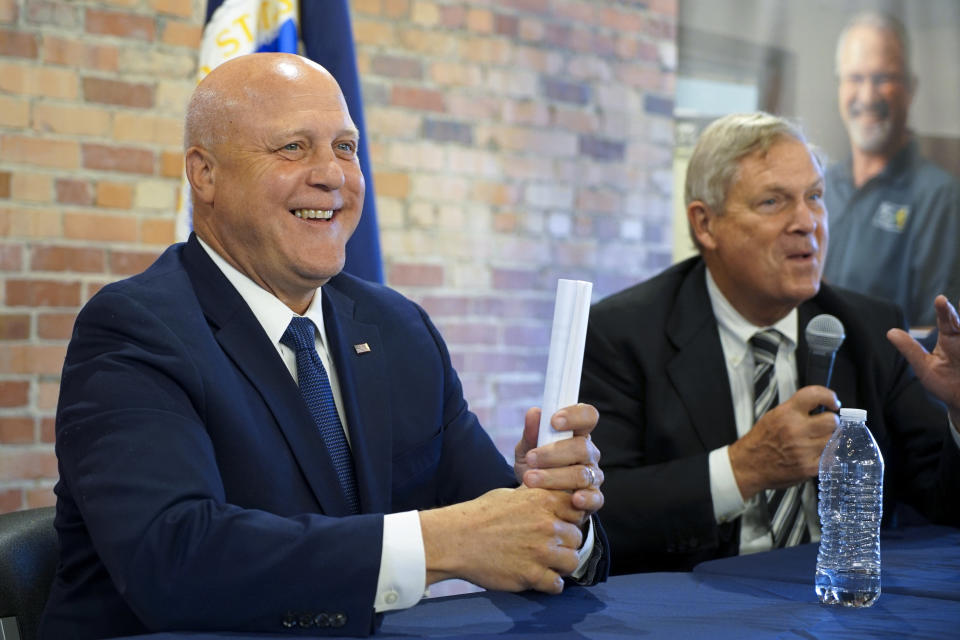 White House senior adviser Mitch Landrieu, left, smiles as U.S. Agriculture Sec. Tom Vilsack speaks in a repurposed railroad depot in Elm City, N.C., during an event to announce rural broadband funding on Thursday, Oct. 27, 2022. AccessOn Networks will receive $17.5 million to connect communities, businesses, farms and educational facilities to high-speed internet. (AP Photo/Allen G. Breed)