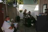 Mario Perez, 32, left, sits on a chair while his wife, Jocelyn, gets her hair bleached at an outdoor hair salon in the Watts neighborhood of Los Angeles, Monday, Aug. 3, 2020. Watts has changed demographically from an exclusively Black neighborhood in the '60s to one that's majority Latino. But it remains a poor neighborhood with high unemployment. (AP Photo/Jae C. Hong)