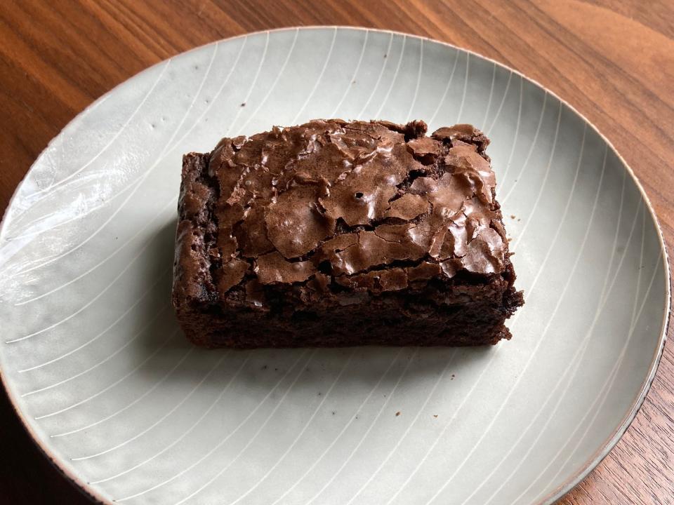 Sliced brownie on a white plate on a wooden table. The brownie has a crackled top