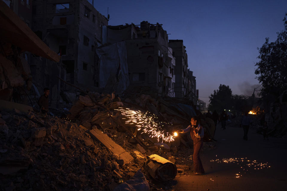 Un niño palestino juega con fuegos artificiales mientras celebra el inicio del mes sagrado del Ramadán junto a un edificio destruido por los bombardeos israelíes en Rafah, en la Franja de Gaza, el domingo 10 de marzo de 2024. (AP Foto/Fatima Shbair)