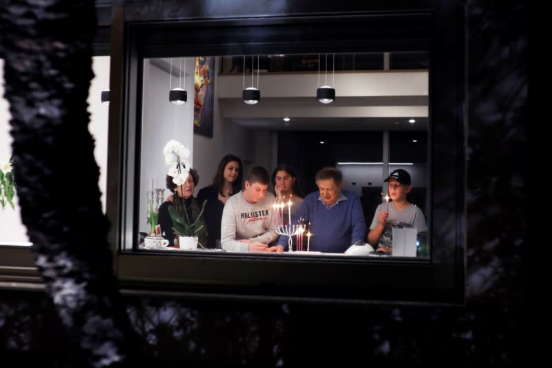 Israeli Holocaust survivor Avraham Harshalom, 95, is seen together with his family through a window as they light a hanukkiyah, a candlestick with nine branches that is lit to mark Hanukkah, the 8-day Jewish Festival of Lights, in Ramat Gan, Is