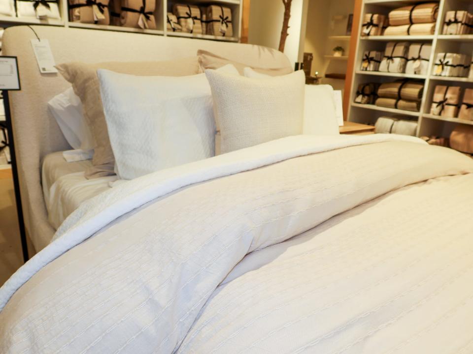 Bedding display with white sheets, a beige comforter, and white and tan throw pillows