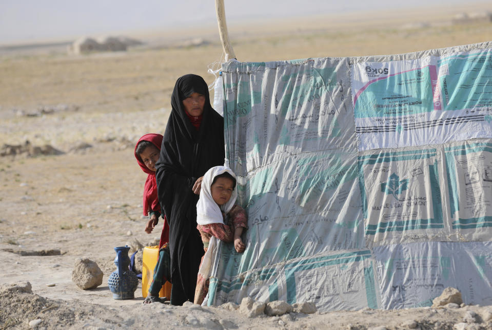 An internally displaced Afghan woman stands with her daughters in front a makeshift tent in a camp on a rocky patch of land, after fleeing fighting between the Taliban and Afghan security personnel, on the edge of the city of Mazar-e-Sharif, northern Afghanistan, Thursday, July 8, 2021. Thousands of people have fled Taliban insurgents sweeping across northern Afghanistan, fearful of their harsh rule. (AP Photo/Rahmat Gul)