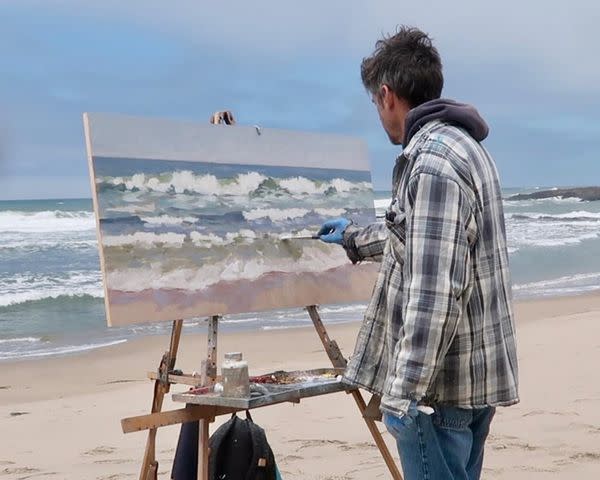 <p>Michael Chamberlain Instagram</p> Michael Chamberlain painting on the beach.