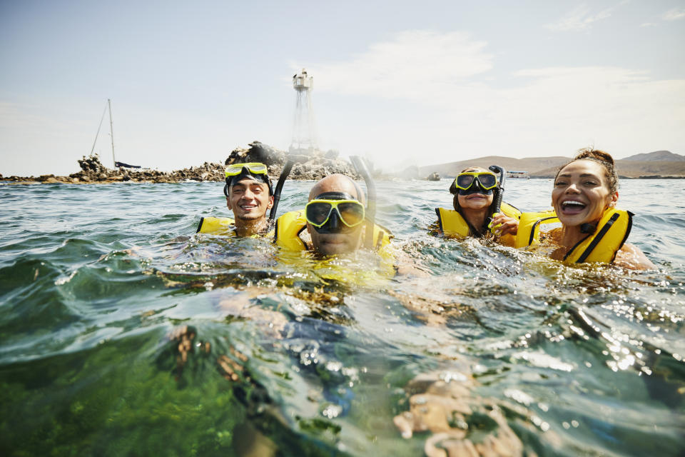 Four people in life vests and snorkeling gear are smiling in the ocean
