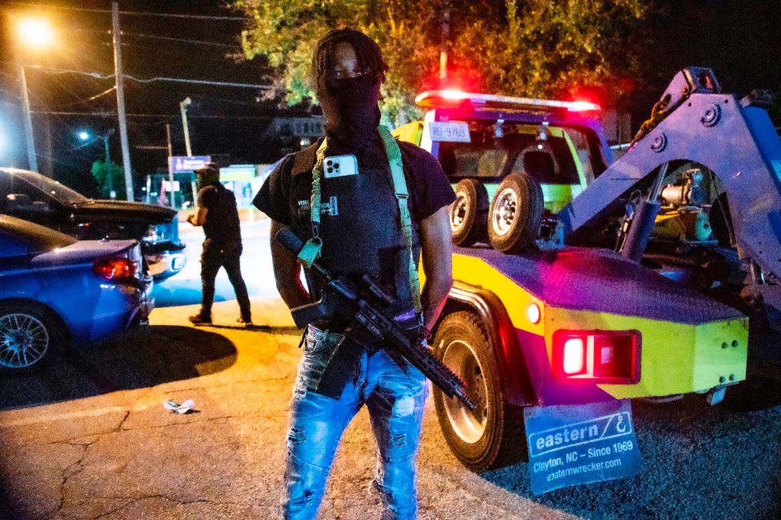 A man who did not want to be identified by stands guard on Peace Street near Glenwood Avenue as tow trucks remove unattended vehicles in a parking lot shortly before 4 a.m. near the Glenwood South district on Friday, July 21, 2023.