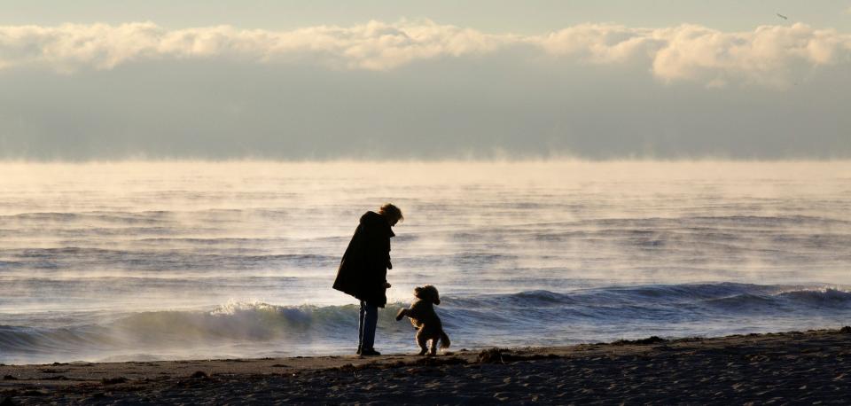 A woman walking Midtown Beach is greeted by a dog as sea fog rises from the ocean off Palm Beach early Monday morning, January 24, 2022.