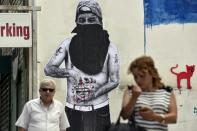 People walk past a mural depicting a person holding a bleeding Euro sign in central Athens on June 25, 2015