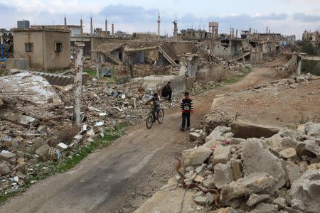 A boy rides a bicycle past a man sitting on rubble of a damaged house in the rebel held historic southern town of Bosra al-Sham, Deraa, Syria, February 23, 2016. REUTERS/Alaa Al-Faqir