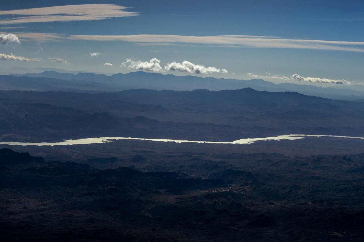 A long-distance view of a river cutting through rugged terrain below a partly cloudy sky