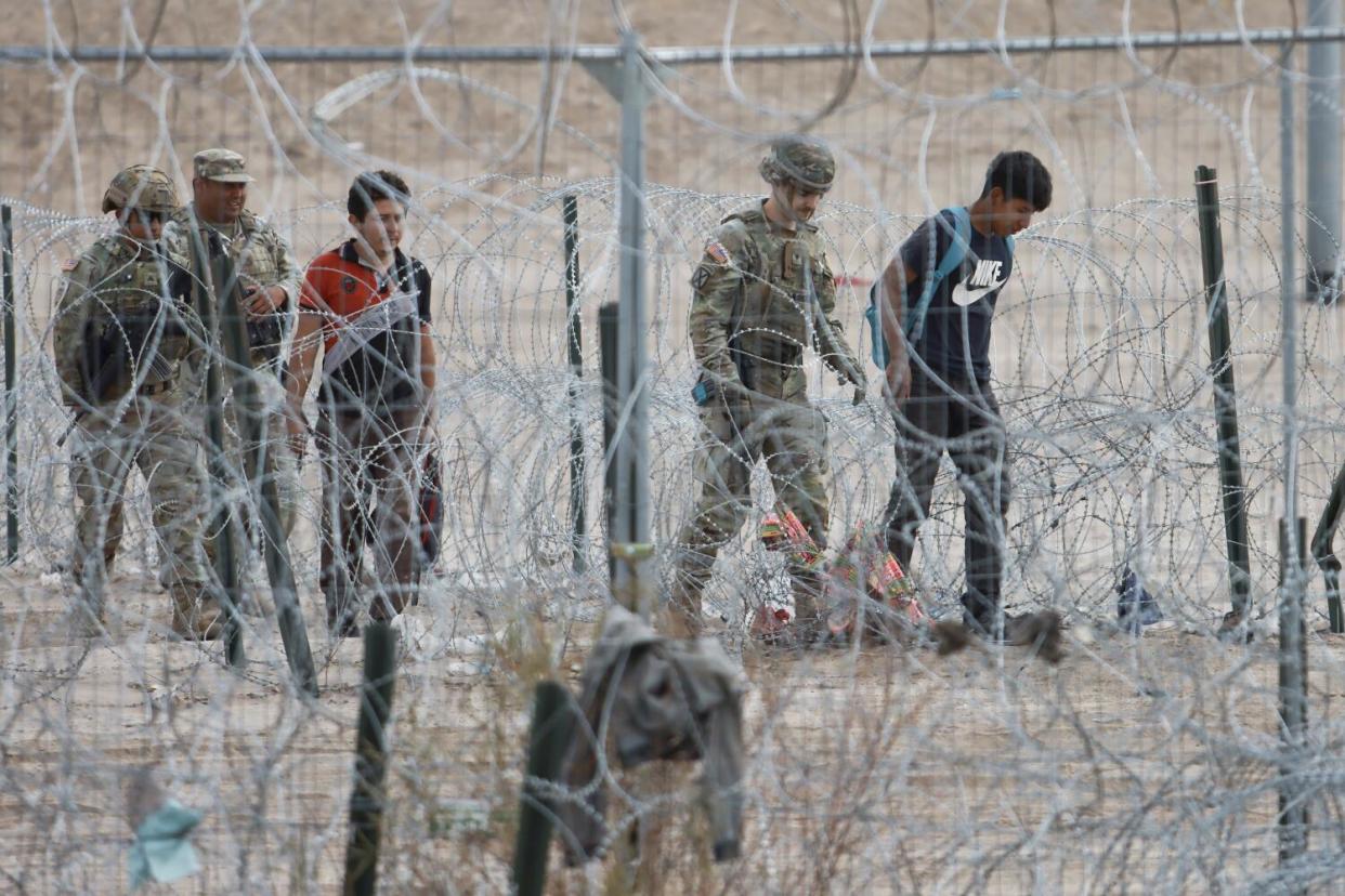 Troops and migrants are seen walking together through razor wire.