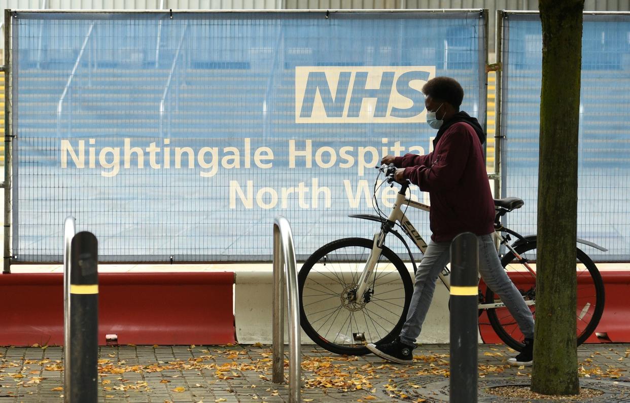 A cyclist wearing a face mask or covering due to the COVID-19 pandemic, pushes a bike past a barrier outside the NHS Nightingale Hospital North West field hospital, set up to provide more hospital capacity during the novel coronavirus pandemic, at Manchester Central Convention Complex in Manchester, northwest England on October 13, 2020. - The National Health Service (NHS) announced that three field hospitals across northern England, in Manchester, Sunderland and Harrogate, would be mobilised to accept new patients amid rising coronavirus infections. The British government faced renewed pressure on October 13 after indications it had ignored scientific advice three weeks ago for tougher restrictions to cut rising coronavirus infections. (Photo by Oli SCARFF / AFP) (Photo by OLI SCARFF/AFP via Getty Images)