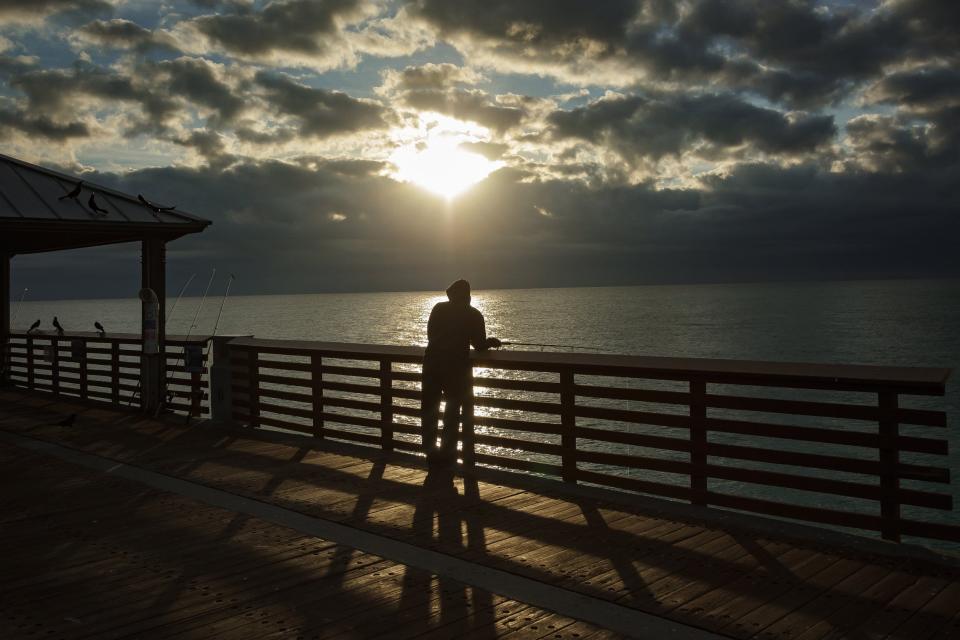 A visitor fishes off the  Juno Beach Pier just before sunrise in Juno Beach.