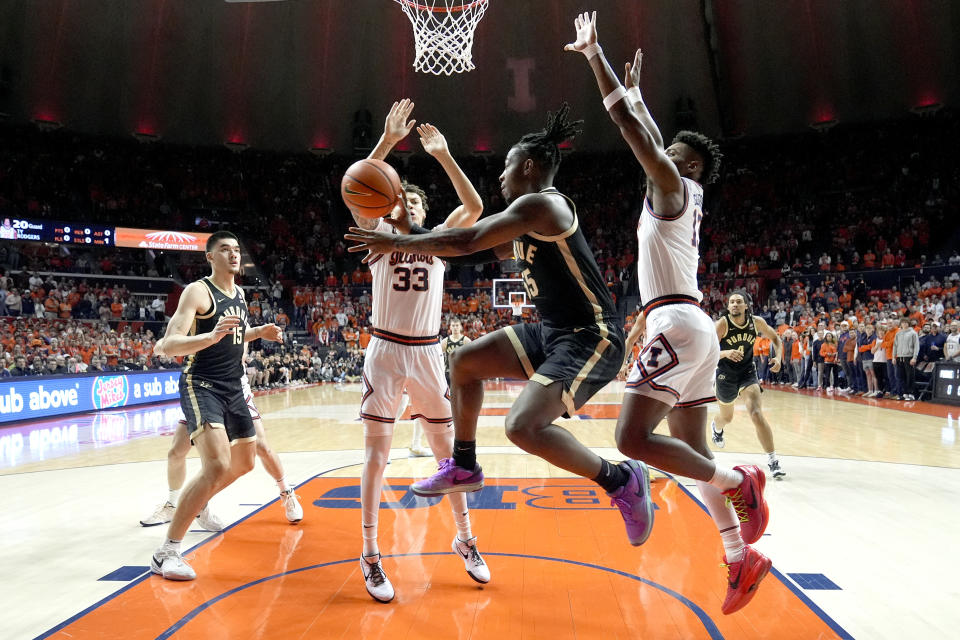 Purdue's Lance Jones passes under the basket as Illinois' Coleman Hawkins (33) and Quincy Guerrier defend during the first half of an NCAA college basketball game Tuesday, March 5, 2024, in Champaign, Ill. (AP Photo/Charles Rex Arbogast)