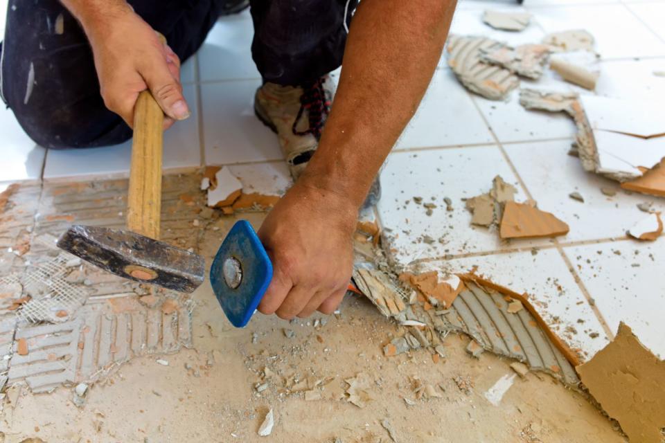 A person is shows breaking the tiles of a bathroom floor during a remodel.