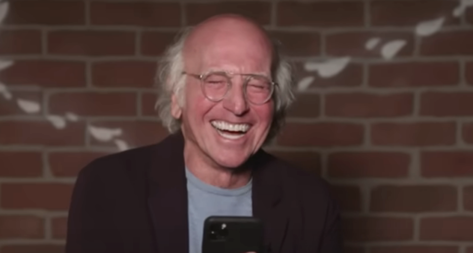 I don't know who is in the image. A man with glasses laughs while holding a smartphone in front of a brick wall