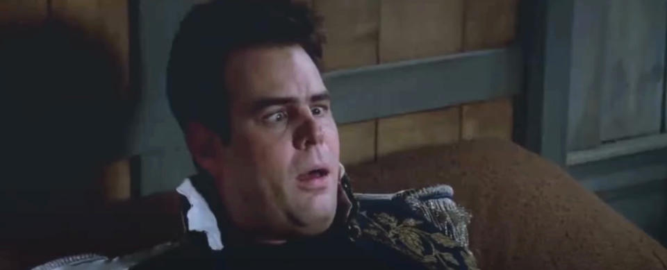 Dan Aykroyd in a scene from the movie "Trading Places," looking surprised and lying on a bed in formal attire