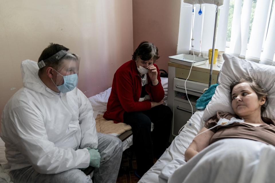 In this photo taken on Thursday, May 28, 2020, Father Yaroslav Rokhman, Ukrainian Greek Catholic Church priest, wearing protective gear to protect against coronavirus, seals to Galina Shamineva, 34, right, dying of cancer, at a hospice in Ivano-Frankivsk, Ukraine. Rokhman, a priest in the Ukrainian Greek Catholic Church, is pleased to be able to return to performing one of a cleric's most heartfelt duties. As the coronavirus pandemic's grip on Ukraine slowly recedes, priests received permission on May 22 to again hold services and visit the sick. (AP Photo/Evgeniy Maloletka)