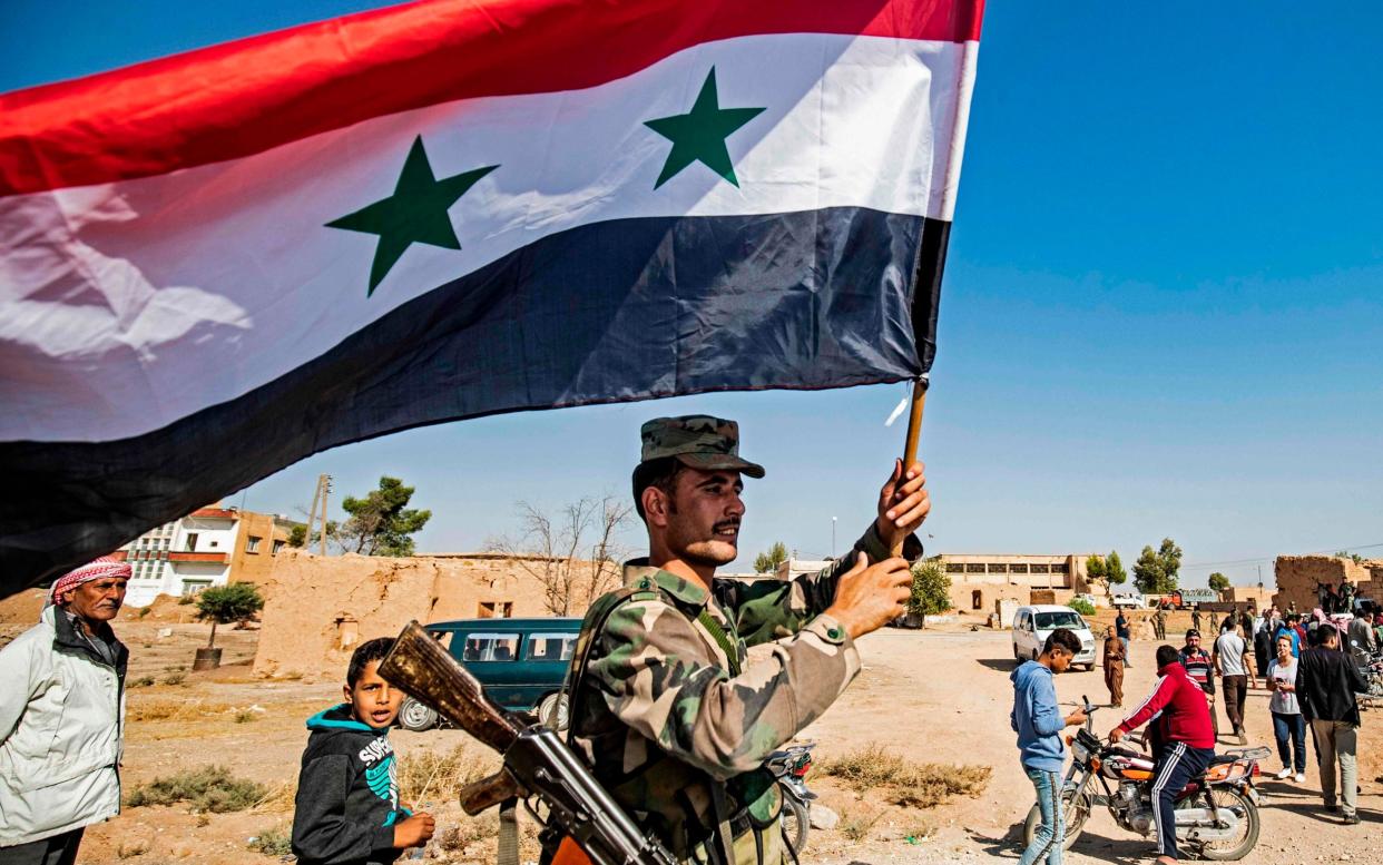 A Syrian regime soldier waves the national flag a street on the western entrance of the town of Tal Tamr in the countryside of Syria's northeastern Hasakeh province on October 14, 2019 - AFP