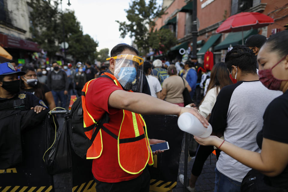 A city worker offers antibacterial gel to passing shoppers as they walk in a crowded commercial district of central Mexico City, Saturday, Dec. 5, 2020. With hospitals once again filling up with COVID-19 patients, Mexico City's mayor on Friday urged people to stay at home as much as possible and authorized checkpoints to limit the number of people entering the capital's colonial-era downtown at one time. (AP Photo/Rebecca Blackwell)