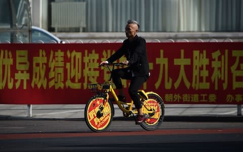 A man rides a sharing bicycle past a promotion billboard for China's 19th Party Congress in Beijing - Credit: AFP