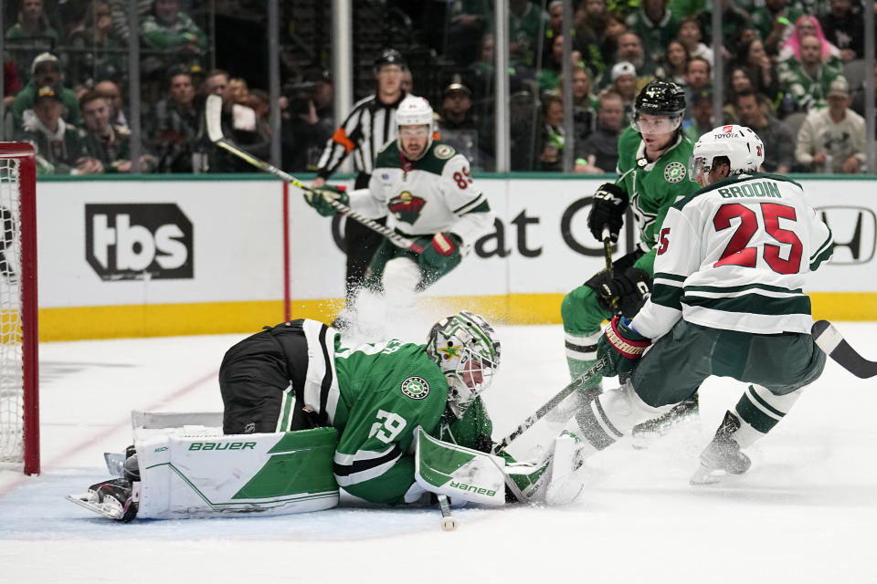 Dallas Stars goaltender Jake Oettinger, left, covers up a shot under pressure from Minnesota Wild defenseman Jonas Brodin (25) during the second period of Game 5 of an NHL hockey Stanley Cup first-round playoff series Tuesday, April 25, 2023, in Dallas. (AP Photo/Tony Gutierrez)