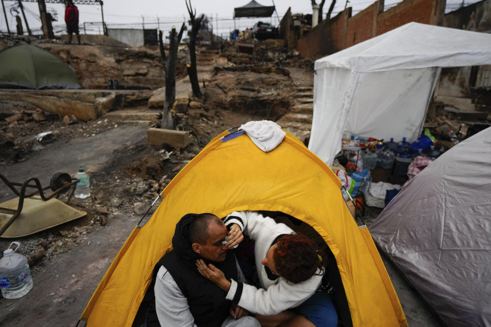 Franchesca Mori limpia la cara de su pareja Miguel Alcaino después de acampar para pasar la noche en el lugar donde estaba su casa antes de ser destruida por un incendio forestal en el barrio Villa Independencia de Viña del Mar, Chile, el martes 6 de febrero de 2024. (AP Foto/Esteban Felix)