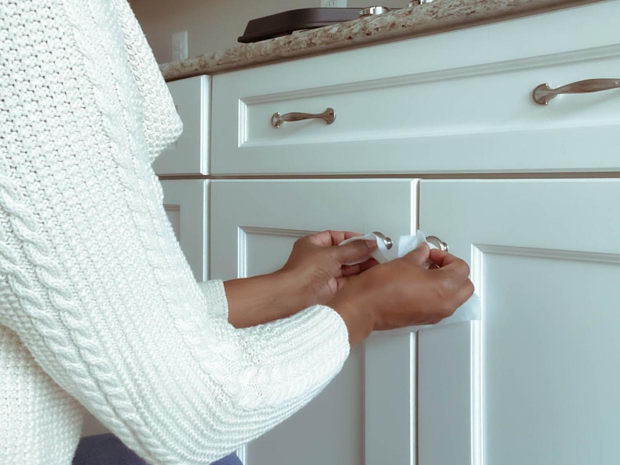 woman cleans cabinet hardware using disinfectant wipe