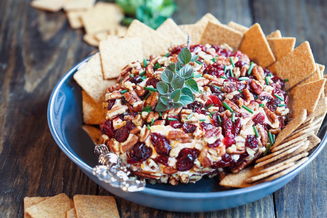 Top view of fresh homemade cranberry cheese spread made with cream cheese, cheddar, dried cranberries, pecans, and chives and garnished with oregano over a rustic wood background. Ready for the holidays.