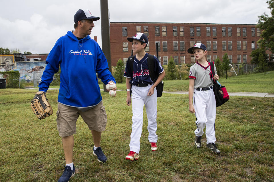 David Fox, from left, walks with his sons Dewey and Jimmy to a nearby baseball field from their house in northeast Washington, Friday, Aug. 23, 2019. David Fox and his wife, Mary Ann, have a rule for their sons, 11-year-old Dewey and 8-year-old Jimmy: They have to play a team sport. The kids get to choose which one. Dewey tried soccer and Jimmy had a go at flag football, but every spring and fall, their first choice is baseball. (AP Photo/Manuel Balce Ceneta)