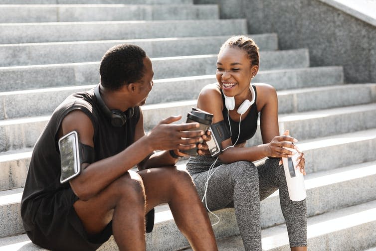 A young man and woman wearing their activewear pause after a workout to drink water and coffee.