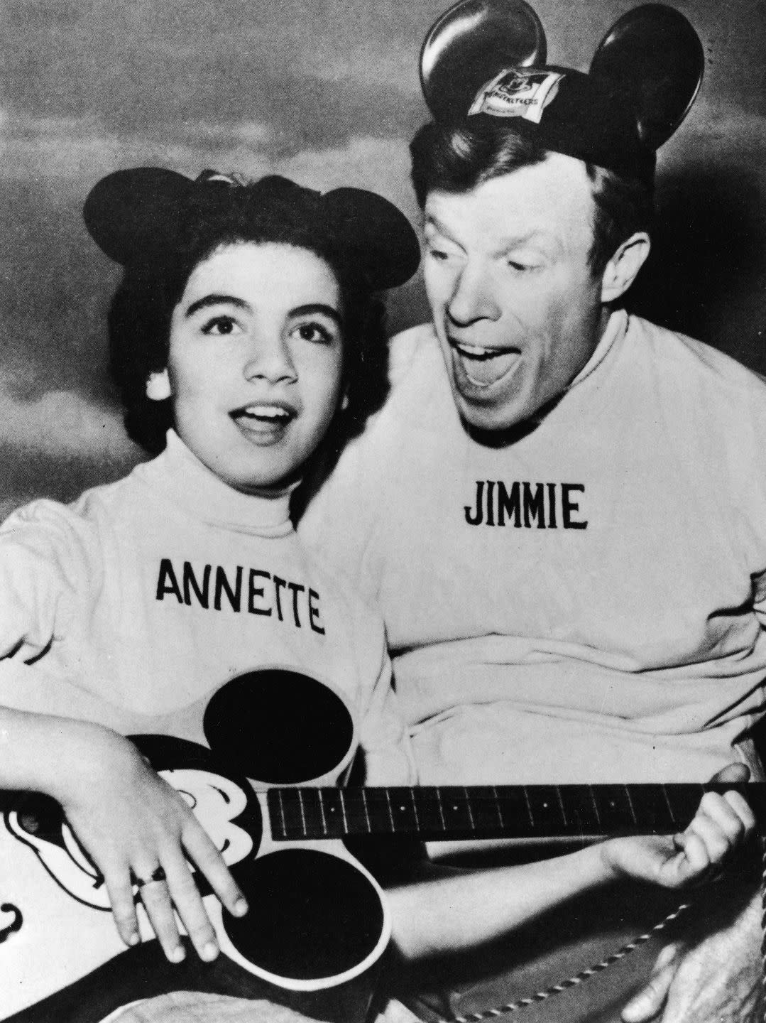 annette funicello plays guitar and sings with jimmie dodd, both wear tops with their names embroidered on them and mickey mouse ear hats