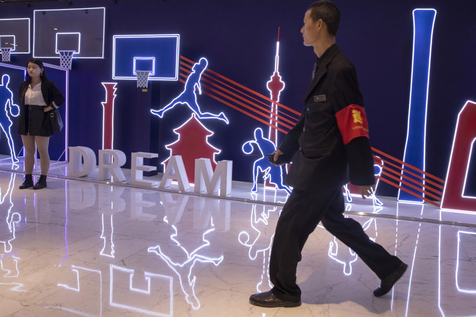 In this Friday, Oct. 11, 2019, photo, a security guard walks past neon light decor depicting basketball players and silhouette of iconic Chinese buildings in Beijing. When Houston Rockets' general manager Daryl Morey tweeted last week in support of anti-government protests in Hong Kong, everything changed for NBA fans in China. A new chant flooded Chinese sports forums: "I can live without basketball, but I can't live without my motherland."(AP Photo/Ng Han Guan)