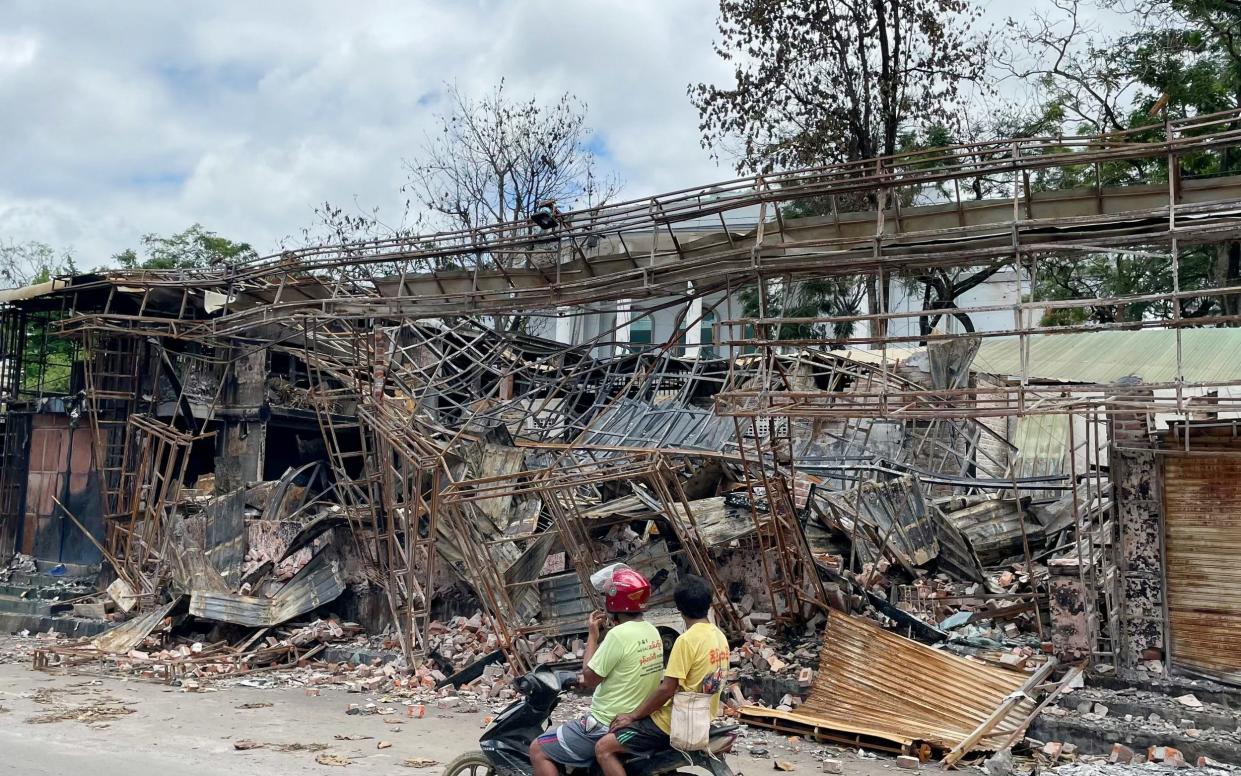 Men on a moped ride past a burnt-out building in Lashio in Myanmar's northern Shan State