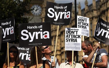 Demonstrators hold placards outside the Houses of Parliament in London in this August 29, 2013 file picture. REUTERS/Suzanne Plunkett