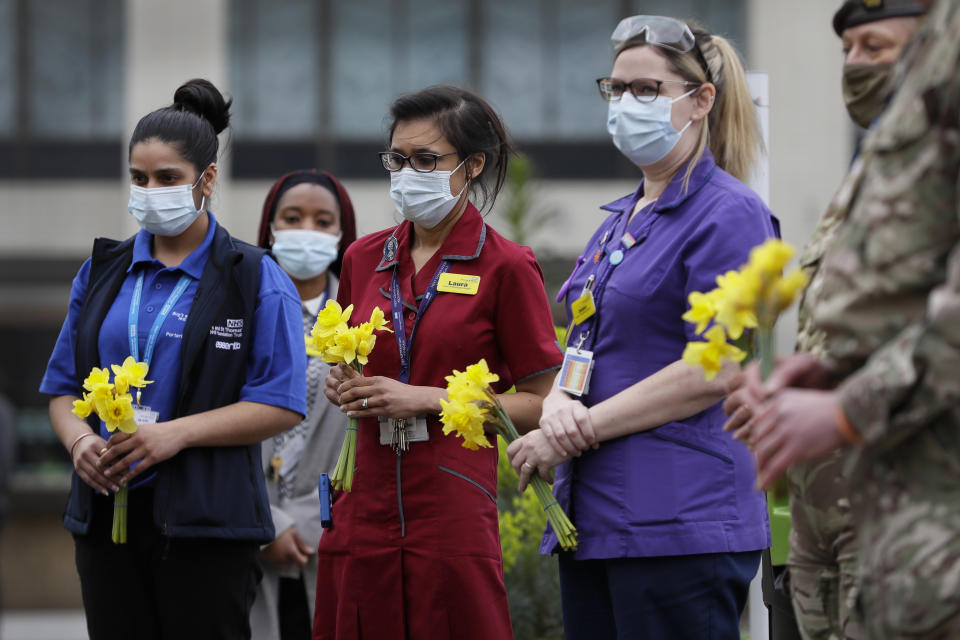 Members of NHS staff hold flowers as they gather for a minute of silence and reflection at St Thomas' hospital in London, Tuesday, March 23, 2021. A year to the day since Prime Minister Boris Johnson first put the country under lockdown to slow the fast-spreading coronavirus, a national day of reflection is being organized to remember the people who died after contracting COVID-19.(AP Photo/Kirsty Wigglesworth)