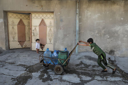 A boy pushes water containers along a street in eastern Mosul, Iraq, April 19, 2017. REUTERS/Marko Djurica