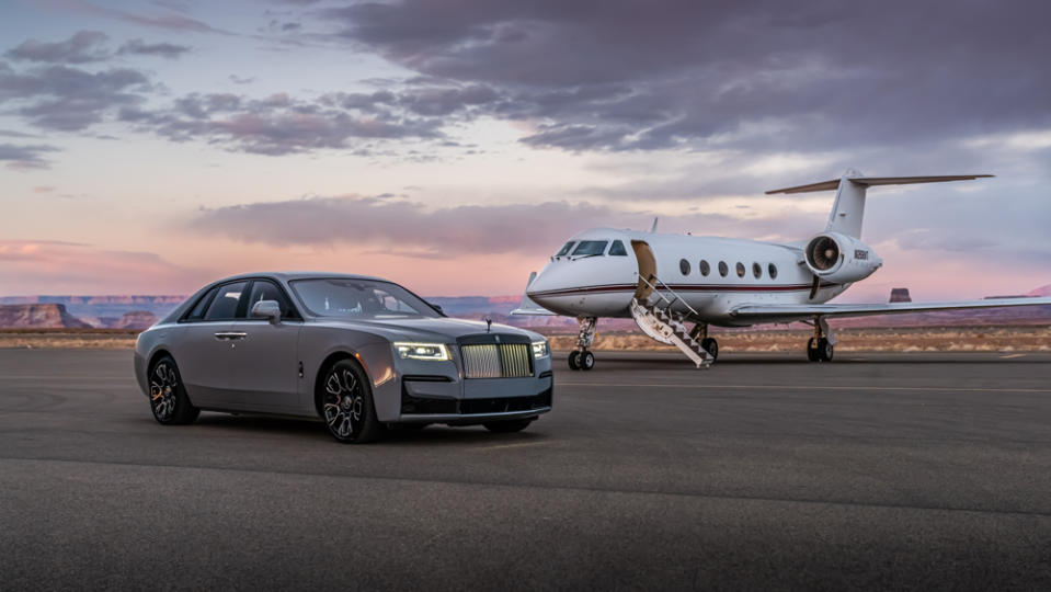 A Rolls-Royce Black Badge Ghost parked in front of a private jet.