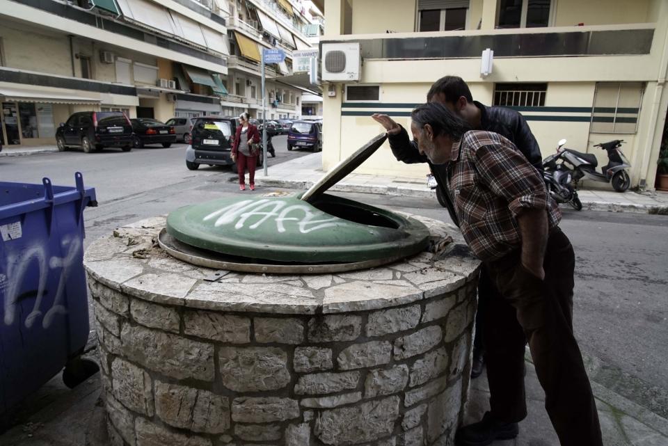 Local residents look inside a garbage dumpster in Kalamata, southern Greece, Wednesday, Dec. 18, 2019. Greek police say they have arrested a 24-year-old foreign woman on suspicion of attempted infanticide after a passer-by found a days-old baby inside this in-ground garbage dumpster. (AP Photo/Nikolia Apostolou)