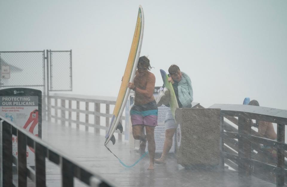 Surfers use their boards to block the rain and wind as the outer bands of Hurricane Idalia pass at Naples Pier in Naples on Tuesday, Aug. 29, 2023.