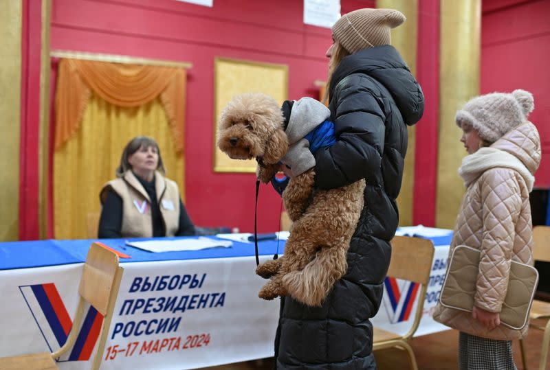 Una votante sostiene un perro mientras espera a recibir su papeleta de un miembro de la comisión electoral en un colegio electoral el último día de las elecciones presidenciales en Omsk, Rusia