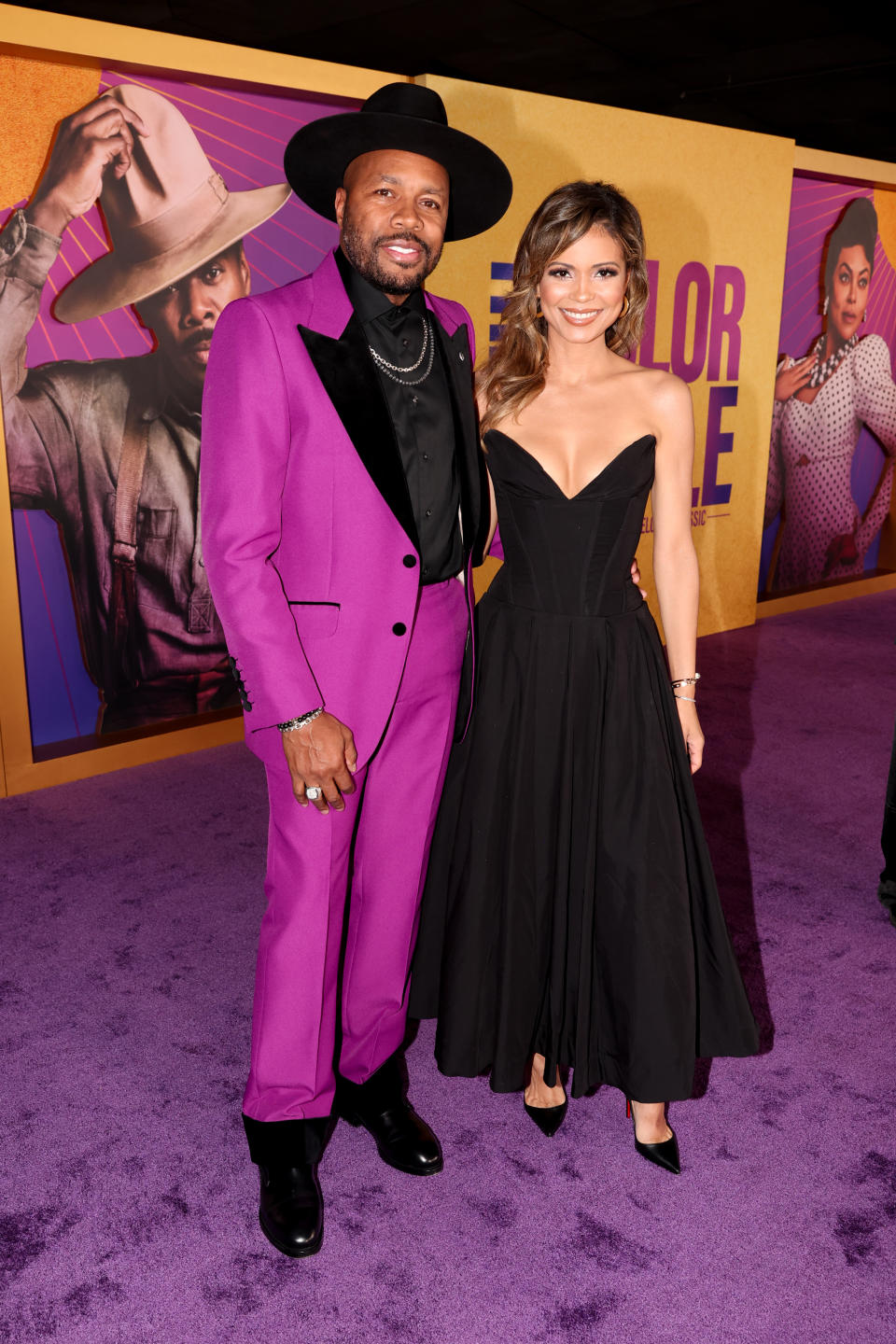 D-Nice in a purple suit with black accents, a black hat, and black shirt, and Jennifer in a strapless flared black gown